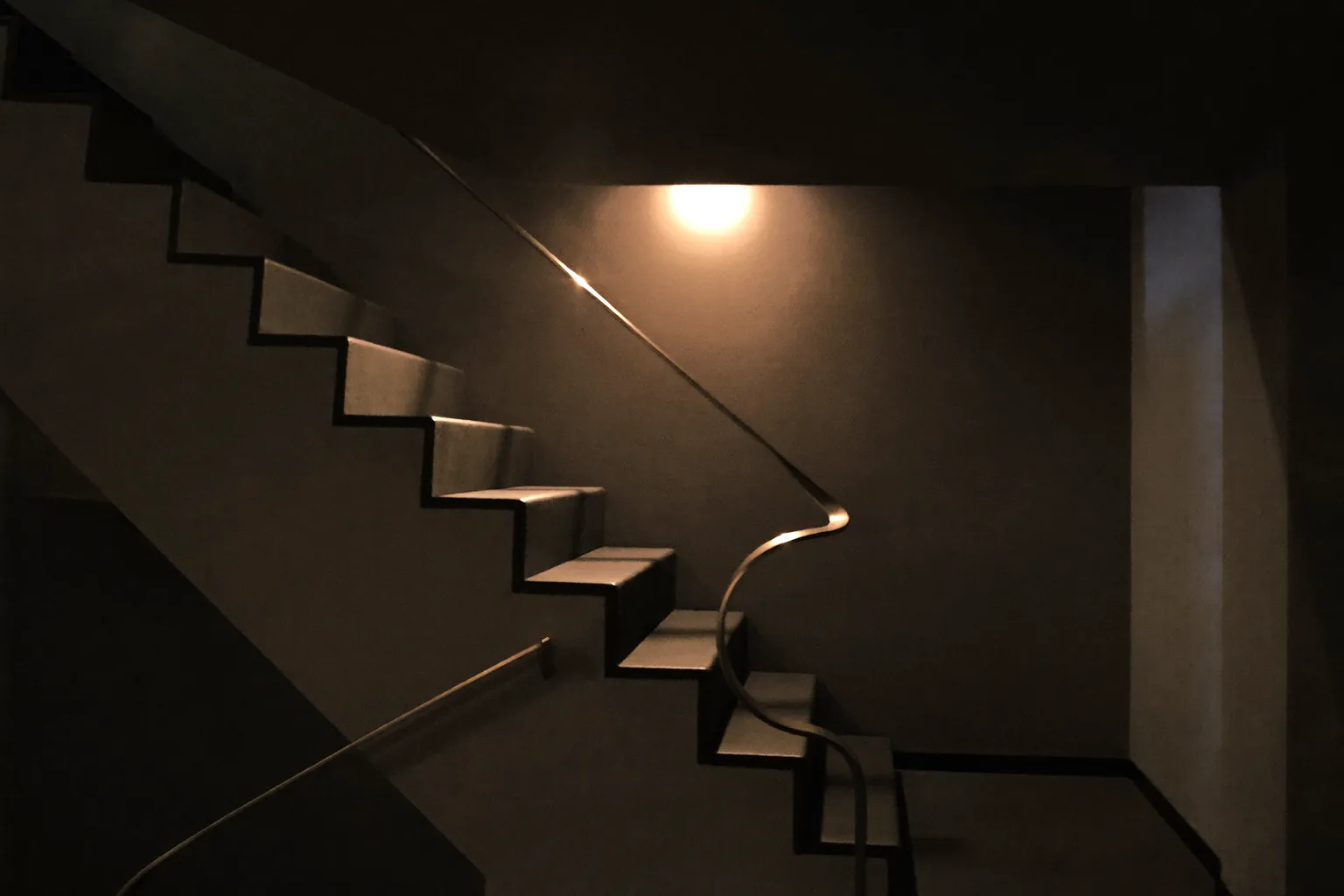 Stairwell with a gold handrail rising toward a warm light
